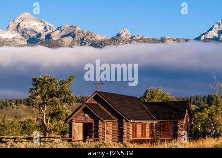 Grand Teton Bergkette und den bischöflichen Kapelle der Verklärung bei Sonnenaufgang, am frühen Morgen Licht getaucht mit Nebel und tiefliegenden Wolken. Stockfoto