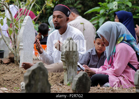 Lhokseumawe, Indonesien. 16 Juni, 2018. Ein paar gesehen Beten neben einem Grab während der Wallfahrt. Muslime mit Grab ihrer Verwandten" während einer Pilgerreise gesehen an den öffentlichen Friedhof in Lhokseumawe Stadt. Die meisten Muslime in Aceh bereits die letzte Grab Wallfahrt vor dem Betreten des heiligen Monats Ramadan und am Tag des Eid al-Fitr, für die Familien der Verstorbenen zu beten. Credit: Maskur hat/SOPA Images/ZUMA Draht/Alamy leben Nachrichten Stockfoto