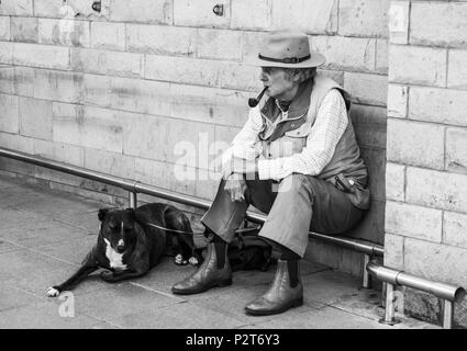 Ein älterer Mann, mit einem Rohr in den Mund, setzte sich außerhalb eines Shop mit seinen alten Hund an seiner Seite am Barnard Castle, England, UK. In Schwarzweiß. Stockfoto