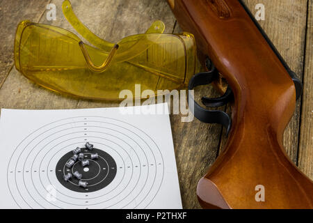 Schießen und pneumatische Waffe. Schild und Hits mit Blei Kugeln auf einem Holztisch. Der dunkle Hintergrund. Stockfoto