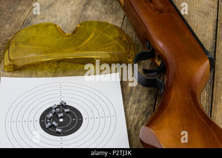 Schießen und pneumatische Waffe. Schild und Hits mit Blei Kugeln auf einem Holztisch. Der dunkle Hintergrund. Stockfoto