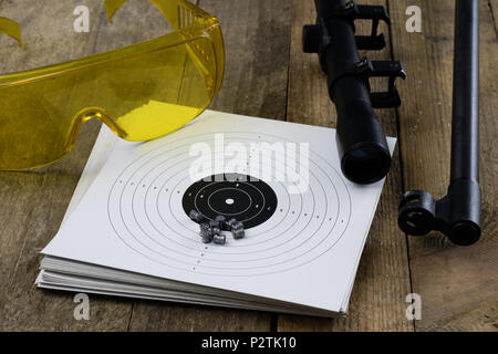Schießen und pneumatische Waffe. Schild und Hits mit Blei Kugeln auf einem Holztisch. Der dunkle Hintergrund. Stockfoto