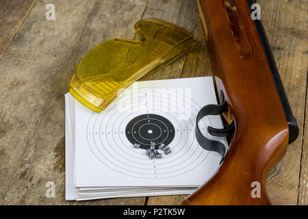 Schießen und pneumatische Waffe. Schild und Hits mit Blei Kugeln auf einem Holztisch. Der dunkle Hintergrund. Stockfoto