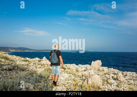 Mann mit Tasche auf der Rückseite stehen auf der felsigen Küste in Kroatien. Auf der Suche nach schönen blauen Adria. Schönen warmen Sommerabend bei Sonnenuntergang. Ruhig, peacef Stockfoto