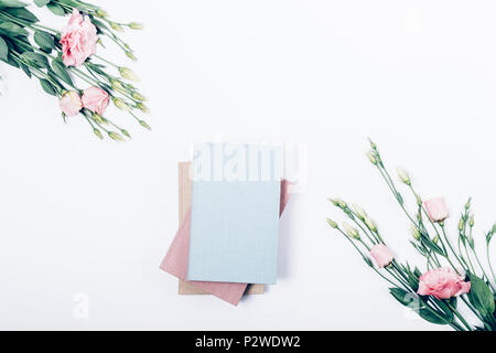 Stapel von drei Bücher auf weißem Hintergrund in der Mitte der Blumen Rahmen, Ansicht von oben. Flach mit Blumensträuße rosa eustomas und Notebook Stockfoto