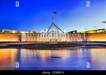 Fassade des neuen Parliament House in Canberra auf dem Capitol Hill bei Sonnenuntergang mit helle Beleuchtung in unscharfer Gewässern der Pool. Stockfoto