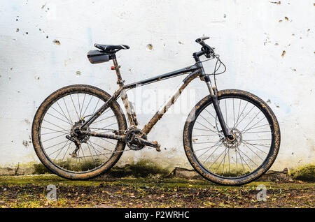 Dirty Mountainbike bedeckt mit Schlamm nach dem Reiten bei schlechtem Wetter steht. Grau 29er Hardtail Fahrrad auf weißer Wand Hintergrund Stockfoto