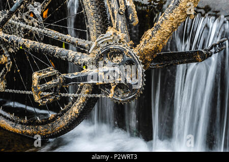 Dirty Mountainbike steht in einem Creek gegen den kleinen Wasserfall. Dirty Kettenantrieb Mountainbike close-up. Reinigung ein Fahrrad Konzept Stockfoto