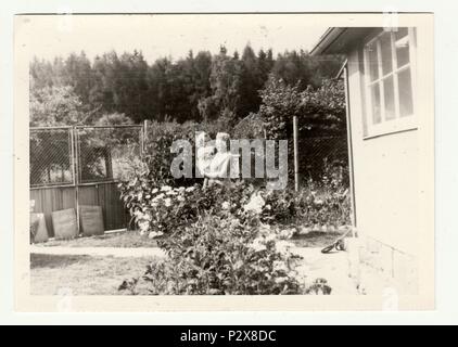 Die tschechoslowakische SOZIALISTISCHE REPUBLIK - circa 1970 s: Vintage Foto zeigt Großmutter wiegen ein kleines Mädchen im Garten. Retro Schwarz/Weiß-Fotografie. Stockfoto