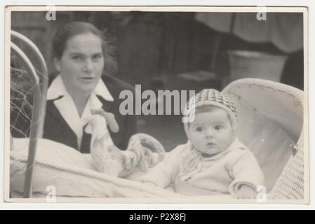 Die tschechoslowakische SOZIALISTISCHE REPUBLIK - circa 1970 s: Vintage Foto zeigt Mutter und ihrem Baby im Kinderwagen sitzt (Schlitten). Retro Schwarz/Weiß-Fotografie. Stockfoto