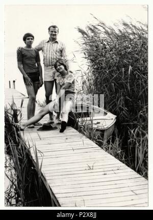 Große Seen in Mecklenburg, Deutschland - AUGUST 1977 - Vintage Foto zeigt Vater und Jugendliche (Jugendliche) Kinder auf dem Pier darstellen. Der Steg und Boot - Sommerferien (Urlaub). Stockfoto