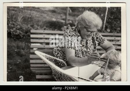 Die tschechoslowakische SOZIALISTISCHE REPUBLIK - circa 1950s: Vintage Foto zeigt Großmutter mit einem kleinen Baby im Kinderwagen (Schlitten). Großmutter hält Abacus. Retro Schwarz/Weiß-Fotografie Stockfoto