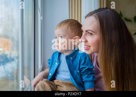 Junge Mutter und nachdenkliche kleine Junge Blick durch Fenster Stockfoto