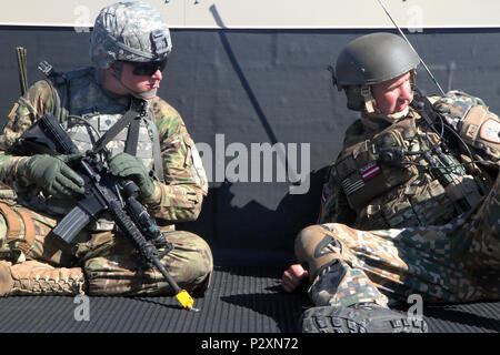 Ein Soldat von Charlie Company 1st Battalion, 125Th Infanterie Regiment in Wyoming, und ein Soldat aus dem Lettischen Landstreitkräfte Infanterie Brigade Combat Support Battalion Michigan, beobachten Aktivität von einem Dach während urban Operations Training im Camp Äsche gemeinsame Manöver von Training Center kombinierte Waffen kollektive Training Service als Teil der Übung Northern Strike Aug 8, 2016. Die Ausbildung umfasste taktischen Bewegungen, Sicherheit, gegen Türen, Clearing Zimmer und eine Vielzahl von anderen Schlacht Bohrer. Übung Northern Strike 16 ist ein National Guard Bureau - geförderte Übung uni Stockfoto