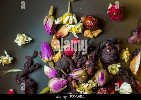 Blumen Tee - Knospen und Früchte von Wild Rose, Kamille und anderen Zutaten in einem keramischen Platte auf einem Holztisch, close-up Stockfoto