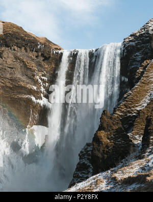 Skógafoss Wasserfall von unten, an einem sonnigen Tag mit einem Regenbogen im Nebel. Portrait Ausrichtung Stockfoto