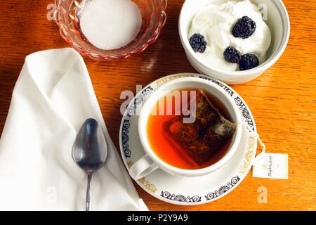 Teetasse und Pudding Dessert mit schwarzen Beeren und einem Tuch Serviette sitzen auf einem Holz Couchtisch mit einem Löffel und Zucker. Stockfoto