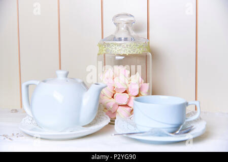 Ein Glas Glas Marshmallow steht hinter einen Wasserkocher und eine Schale auf eine Untertasse mit Spitze. Stockfoto