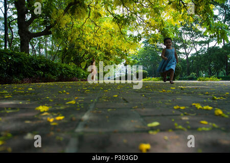 Ein kleines Mädchen läuft unter Sonalu oder Goldene dusche Baum an jatiya Sangsad Bhaban Räumlichkeiten in Dhaka. Dhaka, Bangladesch Stockfoto