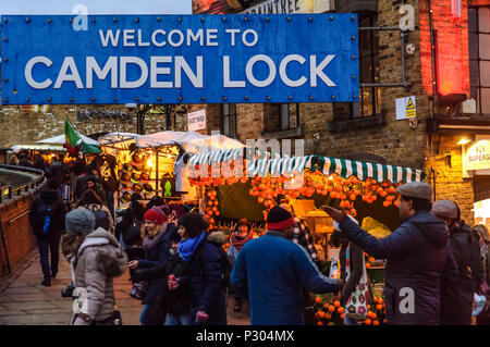 Eingang zum Camden Lock. Die großen blauen Schild "Willkommen in Camden Lock', am Eingang zum Markt. Am frühen Abend, warmem Orange Beleuchtung, und Leute Fräsen um Busy Marktstände. Stockfoto