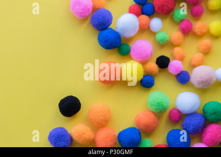 Mehrfarbige pom-poms in verschiedenen Größen auf soliden gelben Hintergrund flach Anordnung Stockfoto
