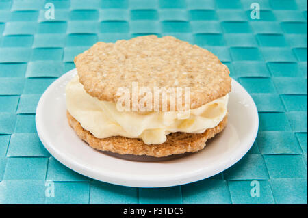 Vanille Eis zwischen zwei oatmeal Cookies auf eine weiße Platte mit einem blauen Hintergrund sandwiched Stockfoto