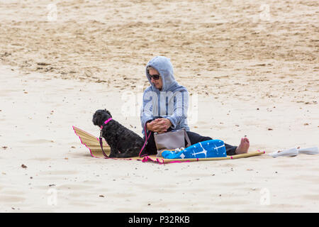 Bournemouth, Dorset, Großbritannien. 17. Juni 2018. UK Wetter: breezy Tag an Alum Chine Beach, nicht davon abhalten, die Besucher zum Meer gehen. Frau sitzt auf Sand mit Hund. Credit: Carolyn Jenkins/Alamy leben Nachrichten Stockfoto