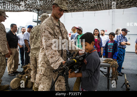 Während der Los Angeles Fleet Week am 1. September 2016 demonstriert ein US-Marine des 3. Bataillons, 5. Marine-Regiment, einem Kind an Bord der USS America (LHA 6), die im Hafen von Los Angeles angedockt ist, die M-249 Squad Automatic Weapon. Die Flottenwoche fördert das öffentliche Verständnis des Marine- und Marinekorps und stellt militärische Ausrüstung, Operationen und Personal vor. Die Veranstaltung konzentriert sich auf Bildung, Engagement der Gemeinschaft und Interaktion zwischen Soldaten und Zivilisten und bietet Einblicke in Waffensysteme und das Leben an Bord eines amphibischen Angriffsschiffs. Stockfoto