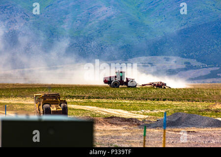 Eine große Staubwolke Fortschritte von einem Traktor schwer am Arbeiten vor Utah Berge. Stockfoto