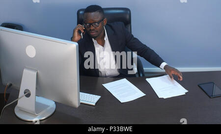 Nachdenkliche junge afro-amerikanischen Geschäftsmann mit einem Telefonanruf, diskutieren Dokumente und im Büro Stockfoto