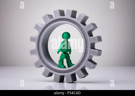 Grüne menschliche Figur zu Fuß auf graue Zahnrad auf weißem Hintergrund Stockfoto