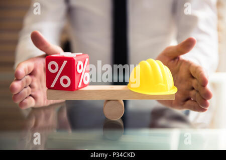 Die schützende Hand Balance zwischen Rot und Gelb Prozentsatz kubische Block Hardhat auf hölzernen Wippe Stockfoto