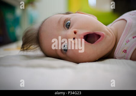 Porträt eines Babys auf dem Bett mit einem überraschten Ausdruck äußerster Bestürzung auf ihrem Gesicht. Stockfoto