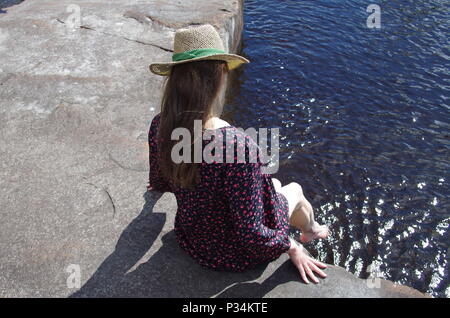 Schöne junge Frau sitzt an einem Fluss ihre Füße ins Wasser. Stockfoto