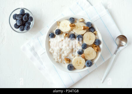 Haferflocken Porridge mit Walnüssen, Blaubeeren und Banane in der Schüssel - gesundes Bio-Frühstück, Hafer mit Früchten, Honig und Nüssen Stockfoto