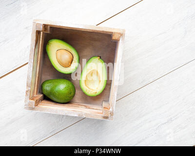 Avocado auf alten Holztisch. Halfs auf hölzerne Schüssel. Obst gesunde Ernährung Konzept. Avocado in einer Holzkiste. Stockfoto