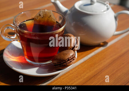 Eine Tasse Tee mit Schokoladenmakaronen, natürliches Licht auf Holztisch Stockfoto