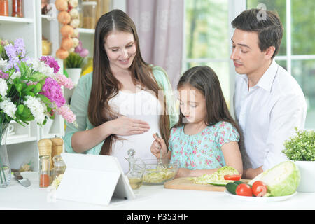 Gerne schwangere Frau mit Mann und Tochter Salat vorbereiten Stockfoto