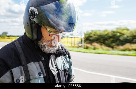 Portrait von älteren Motorradfahrer trägt eine Jacke und Brille mit einem Helm auf sonnigen Sommertag im Freien Nahaufnahme Stockfoto