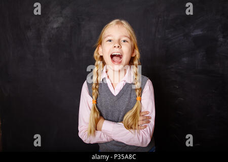 Lustige Schulmädchen auf blackboard Hintergrund Stockfoto