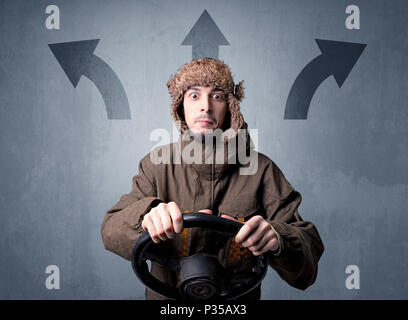 Junger Mann, schwarzes Lenkrad mit drei Pfeilen über seinem Kopf weisen in verschiedene Richtungen. Stockfoto