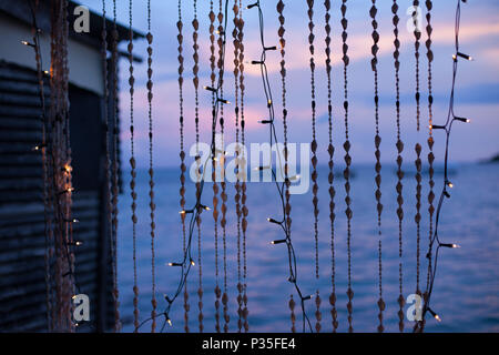 Strings von Muscheln und Weihnachtslichter auf einer tropischen Insel in der Dämmerung Stockfoto