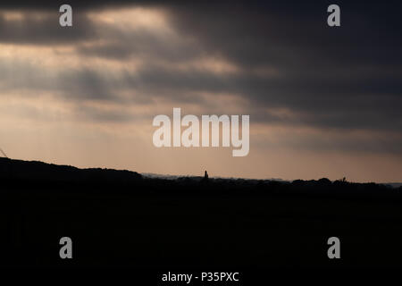 Silhouetten der Büsche und Bäume am Horizont mit Sonnenstrahlen scheinen durch die coulds bei Sonnenuntergang Stockfoto