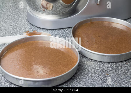 Kuchenformen mit Schokolade Teig und Mixer im Hintergrund Stockfoto