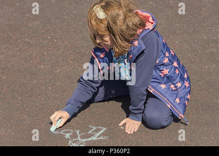 Das Kind malt mit Kreide auf den Asphalt, ein kleines Mädchen in windigen Wetter verschiedenen Beschriftungen schreibt Stockfoto