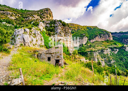 Eine Frau geht ein altes Haus entlang der Weg der Götter, auch als Pfad der Götter bekannt und bietet einen atemberaubenden Blick auf die Küste von Amalfi. Stockfoto