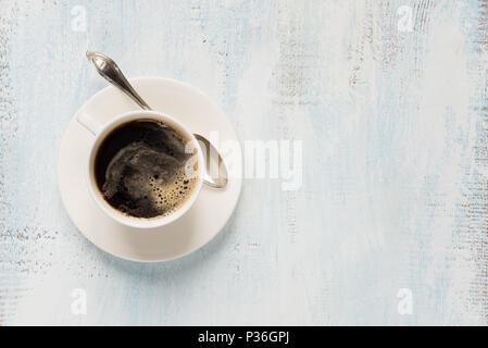 Weißes Porzellan Tasse schwarzen Kaffee mit silberne Teelöffel auf dem hellen Hintergrund mit copy-Raum; Ansicht von oben Stockfoto