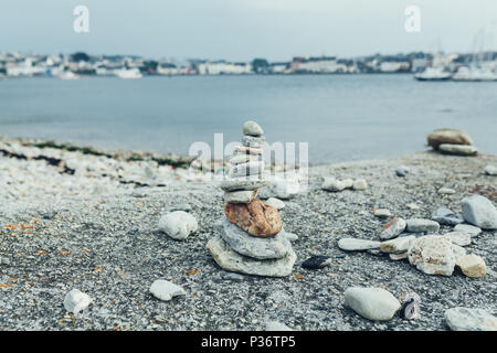 Die Steine der Pyramide auf Kiesel-strand symbolisiert Stabilität, Zen, Harmonie, Balance. Flache Tiefenschärfe mit der Stadt im Hintergrund Stockfoto