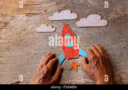 Eine Nahaufnahme von einem älteren Mann mit einer Rakete auf einen hölzernen Tisch. Konzept des Denkens über Kindheitsträume, Traurigkeit und Einsamkeit. Stockfoto