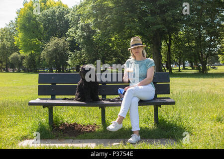 Eine Frau teilt ihr Croissant mit ihrem Hund auf einer Parkbank und genießen Sie einen Kaffee Stockfoto